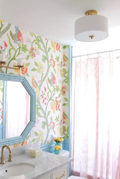 a bathroom with floral wallpaper and blue vanity mirror, gold faucet, white sink, and pink shower curtain