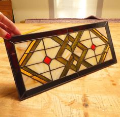 a hand holding a stained glass window on top of a wooden table