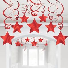 red stars and swirls hanging from the ceiling in front of a white room with windows