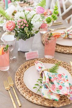 the table is set with pink and white flowers in vases, napkins, and gold utensils