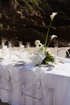 the table is set with clear chairs and white flowers