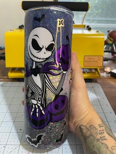 a hand holding a purple and black tumbler with a cartoon character on the side