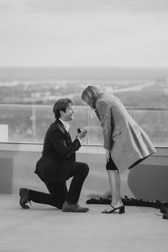 a man kneeling down next to a woman on top of a building while holding a cell phone