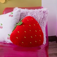 a red strawberry pillow sitting on top of a pink bed