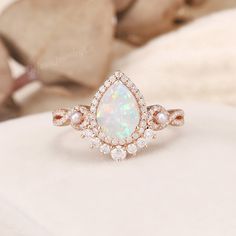 a white opal and diamond ring sitting on top of a bed next to a pillow