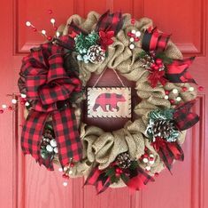 a wreath with a bear and pine cones hanging from it's side on a red door