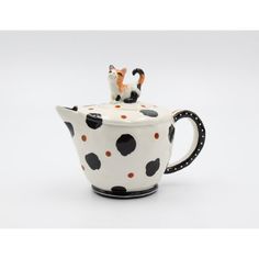 a ceramic teapot with a cat on top and polka dot design, sitting in front of a white background