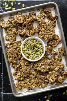 a tray filled with granola next to a bowl of green beans and pumpkin seeds