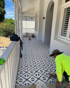 a man in yellow shirt and hat laying tile on porch