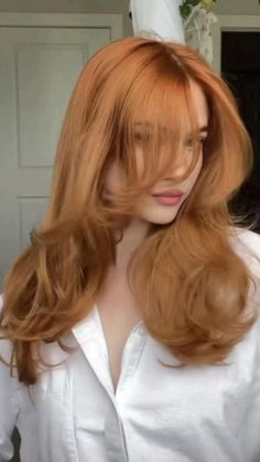 a woman with long red hair standing in front of a mirror wearing a white shirt