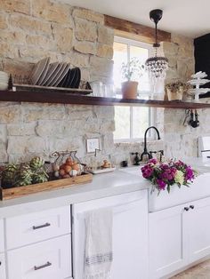 a kitchen with stone walls and white cabinets is pictured in this image, there are flowers on the counter