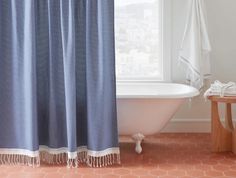 a bath tub sitting next to a window covered in blue shower curtain and tassels