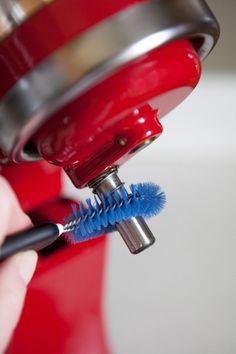 a person is holding a blue toothbrush in their right hand as they use a red blender