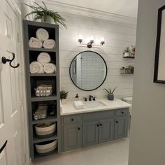 a bathroom with gray cabinets and white towels on the shelves, along with a round mirror