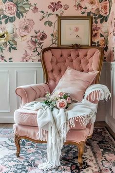 a pink chair sitting in front of a wall with flowers on it and a rug