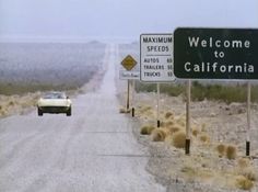 a car driving down a road next to a sign that says welcome to california