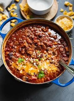 a blue pot filled with chili and cheese on top of a black table next to other dishes