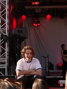 a man sitting on the ground in front of an audience at a music festival with his arms crossed