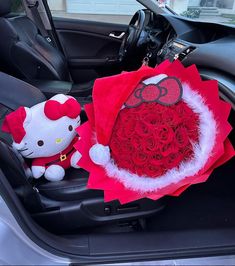 a hello kitty stuffed animal sitting in the back seat of a car next to a bouquet of roses