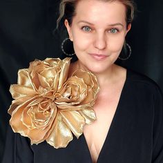 a woman wearing a black top and gold flower brooch on her neck is smiling at the camera