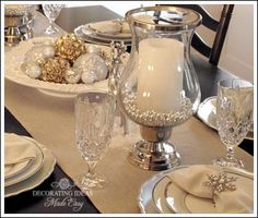 a dining room table set for christmas with silver and white decorations on it, including candlesticks