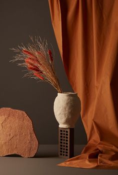 a white vase sitting next to a rock on top of a table with a plant in it