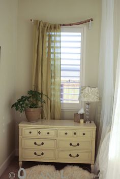 a white dresser sitting under a window next to a green potted plant on top of a table