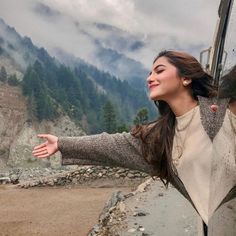 a woman standing in front of a train window with her arms spread out and mountains in the background