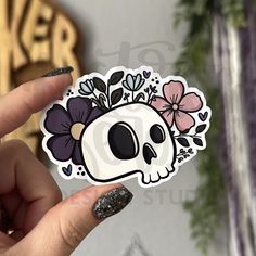 a hand holding up a sticker with a skull and flowers on the back of it