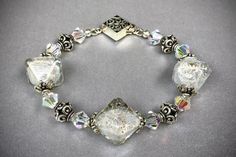 a silver bracelet with glass beads and crystal stones on the clasp is sitting on a gray surface