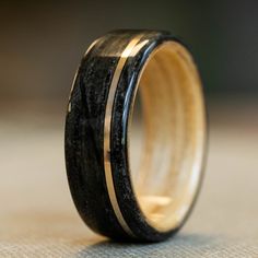 a wooden ring with black and gold inlays sits on top of a table