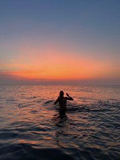 a person in the water with a surfboard at sunset