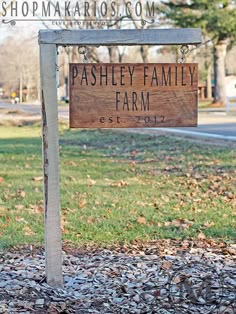 a wooden sign sitting on the side of a road next to a grass covered field