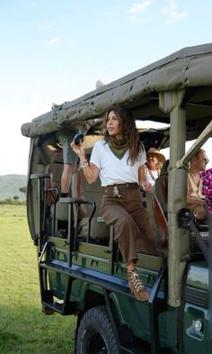 a woman sitting in the back of a green vehicle on top of a lush green field