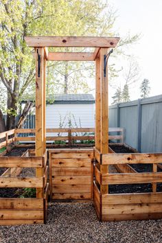 an outdoor garden area with raised wooden planters and trelliss, surrounded by gravel