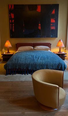 a bedroom with a large painting above the bed and two chairs in front of it