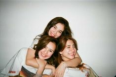 three young women laying on top of each other in front of a white wall with their arms around one another