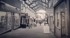 an empty shopping mall with people walking down the walkway and shops on both sides in black and white