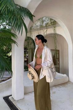 a woman standing in front of a palm tree wearing a white jacket and green pants