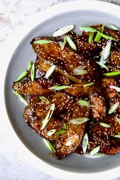 a plate filled with meat covered in sesame seeds and garnished with green onions