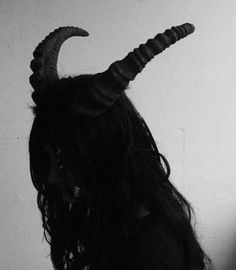 a woman with long hair and horns on her head is looking at the wall behind her