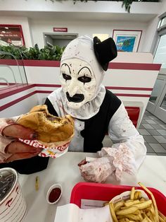 a person in a mask eating a sandwich at a table with fries and ketchup