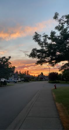 the sun is setting behind some trees on the side of the road with houses in the background