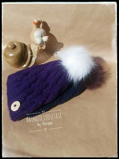 a purple hat with a white fur ball on top and a small toy snail sitting next to it