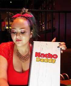 a woman sitting at a table with a notebook in front of her and the words nacho daddy written on it