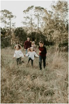 a group of kids are running through the tall grass in an open field with their arms around each other