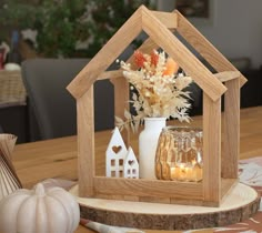 a wooden house shaped candle holder with flowers and candles in it on top of a table