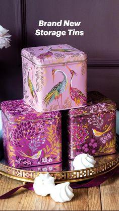 three decorative tins sitting on top of a table next to flowers and a vase