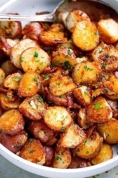 a white bowl filled with cooked potatoes covered in seasoning and garnished with parsley