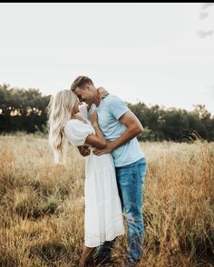 a man and woman standing in the middle of a field hugging each other with trees in the background